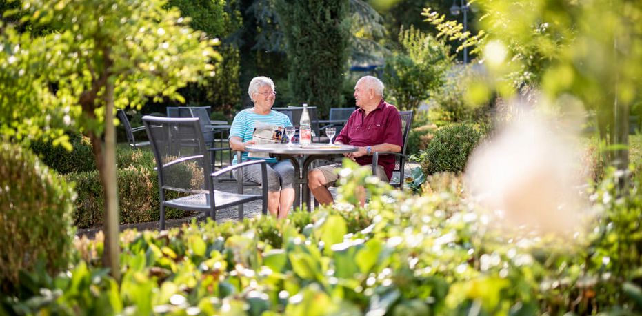 Patienten sitzen im Garten der Klinik und trinken Kaffee