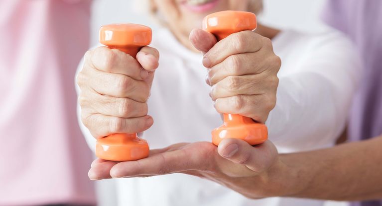 Eine Seniorin trainiert mit kleinen orangefarbenen Gewichten