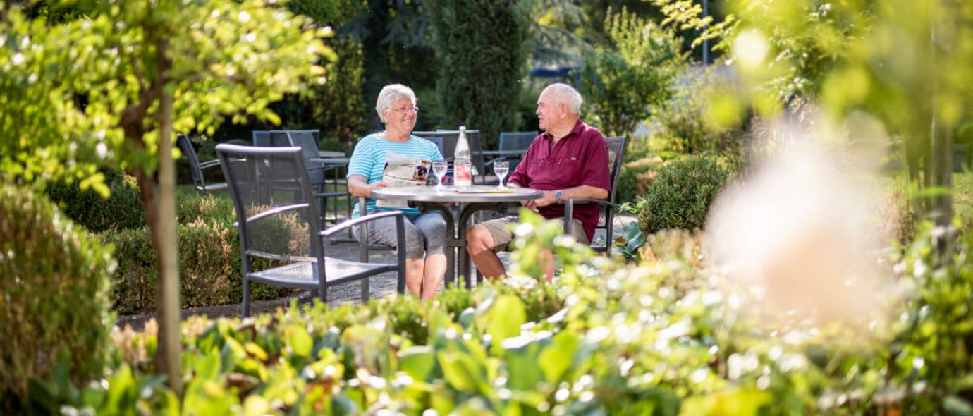 Patienten sitzen im Garten der Klinik und trinken Kaffee