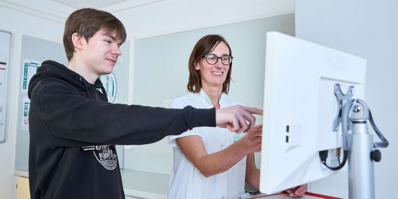 Pflege-Mitarbeiterin und Azubi am Bildschirm
